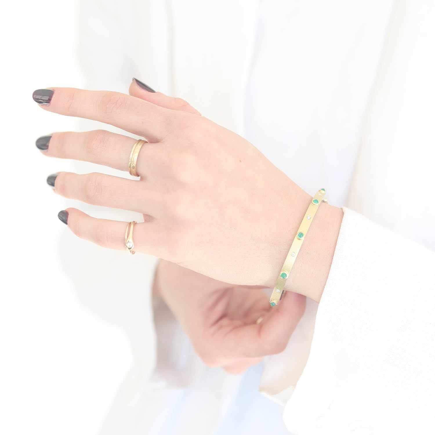 Rene Escobar Trunk Show:31 0.65CT 4MM. SS hinged bangle featuring an 18k YG push button style clasp and a solid 18k YG top sheet and 5 18k YG bezels set with CAB cut 0.65CT of EME